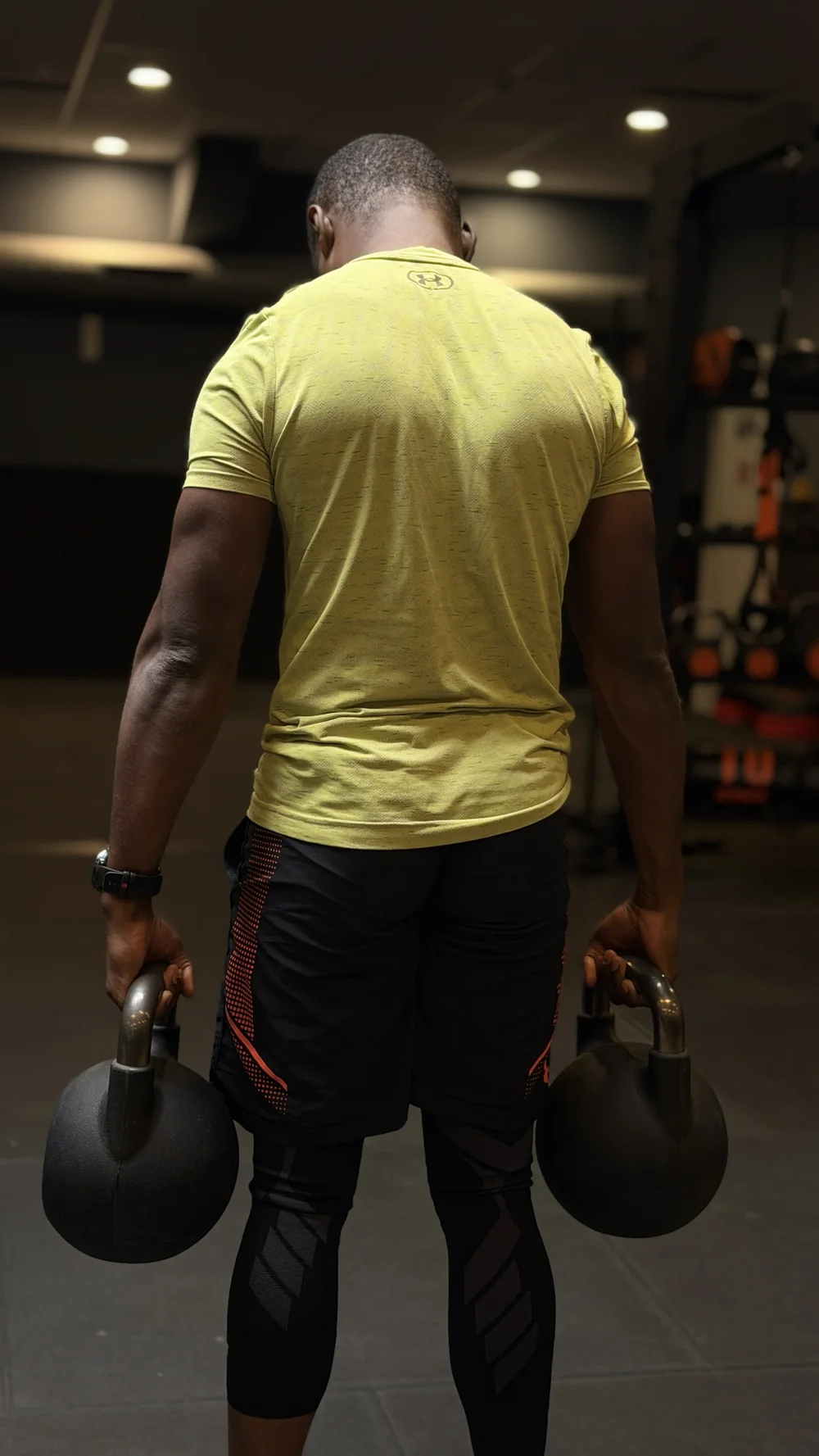 Bouba Ousmana en marche du fermier avec deux kettlebells, vue de dos